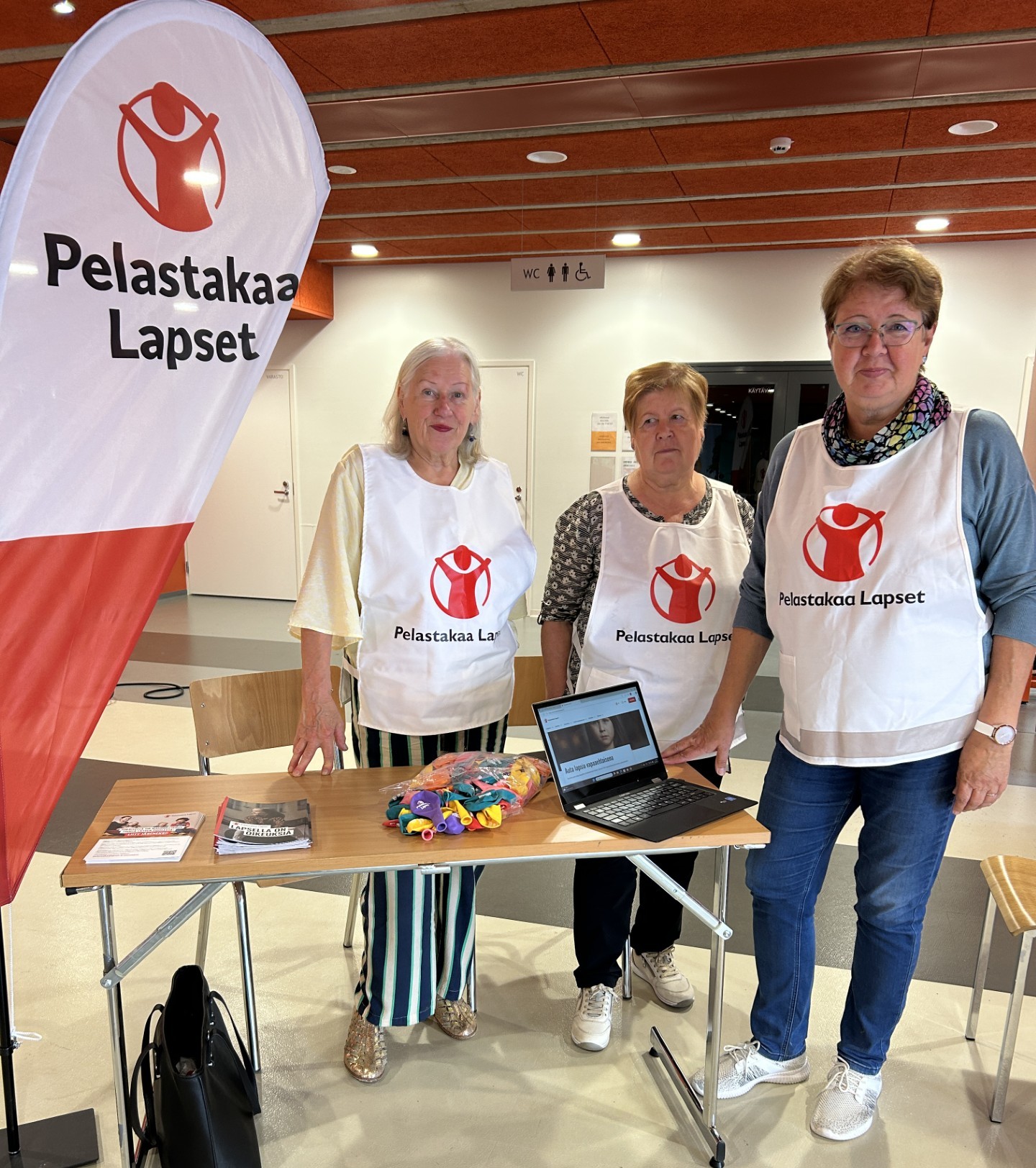 Kolme naista seisoo Pelastakaa Lasten messupisteellä