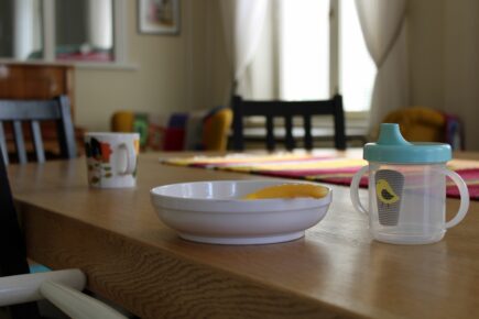 Kuva Perheentalon tuvasta. Pöydällä muoviset lautanen, lusikka ja nokkamuki. Niiden takana aikuisten kahvikuppi.