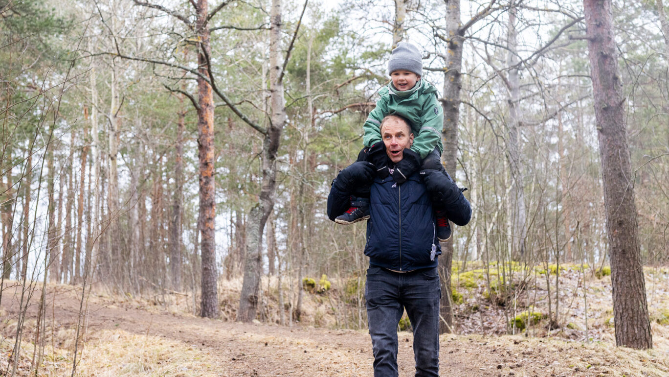 Lapsi istuu aikuisen olkapäillä iloisena metsässä