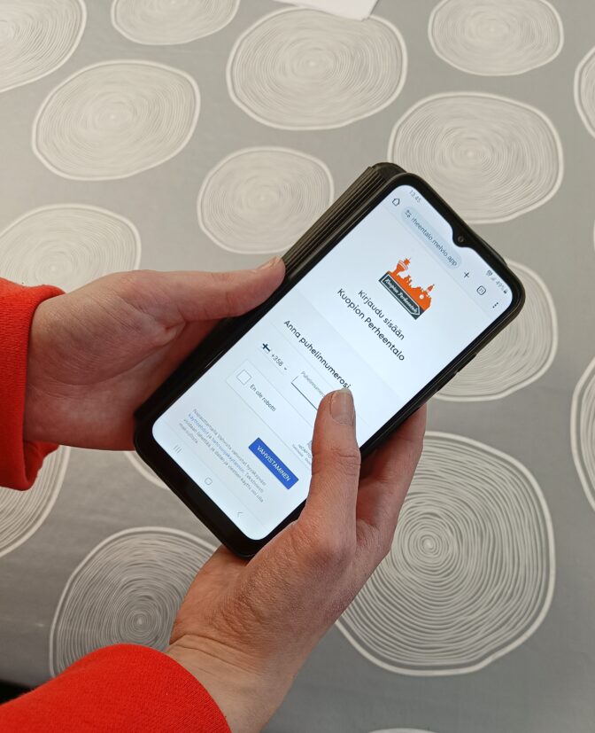 Käsissä puhelin jossa auki Perheentalon jäsensivut