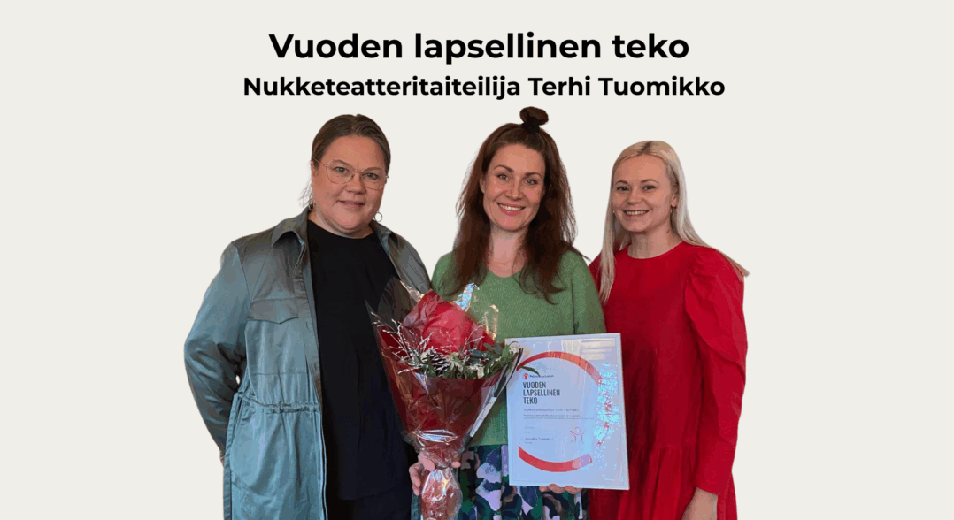 Kuvassa on kolme hymyilevää naista, keskimmäinen on saanut kunniamaininnan ja hänellä on kädessään kehystetty kunniamaininta sekä kukkakimppu. 