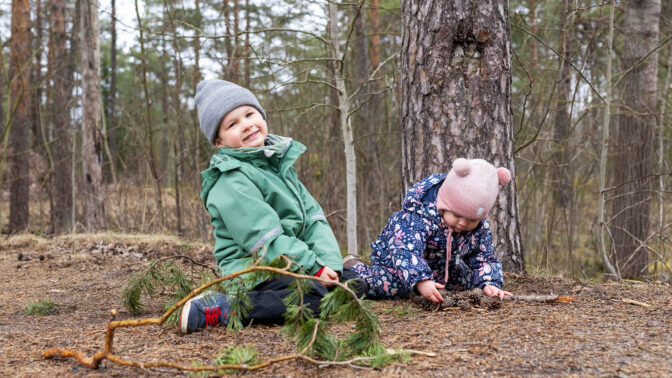 Lapset istuvat iloisena metsässä tutkimassa käpyjä