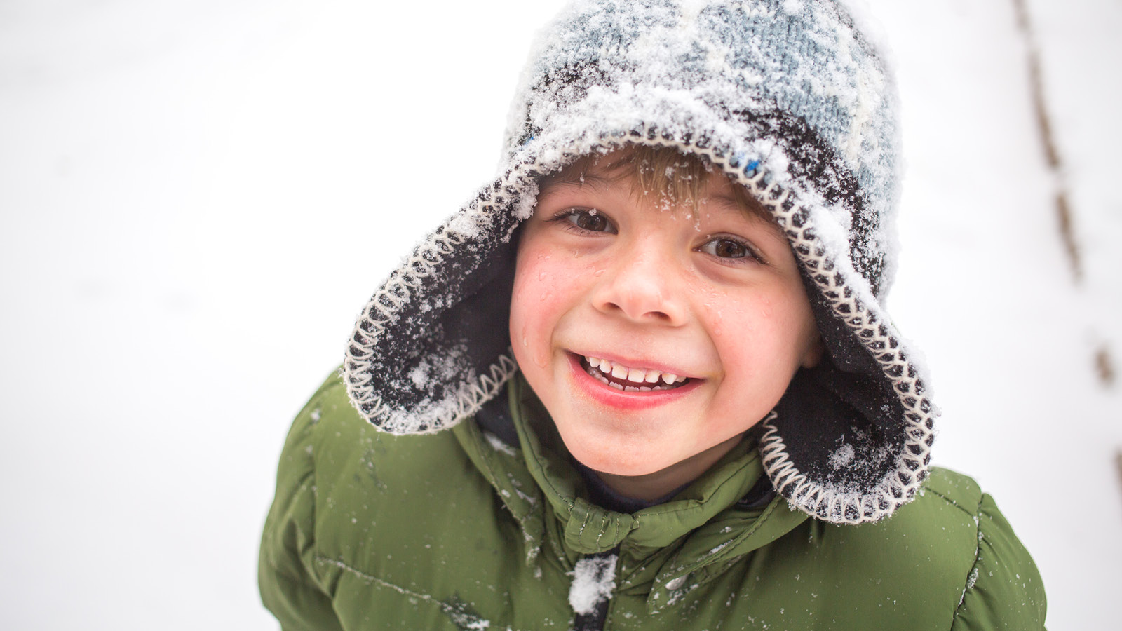 Lapsi hymyilee talvisessa maisemassa ja hänellä on pipo aivan luminen