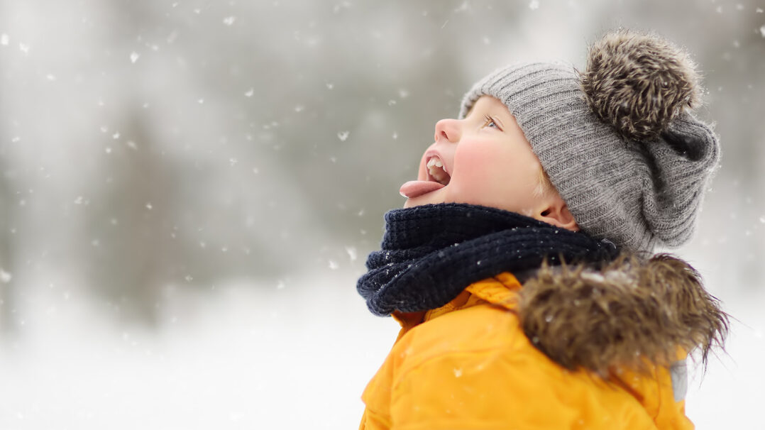 Lapsi seisoo lumisateessa suu auki yrittäen napata suuhun lumihiutaleita