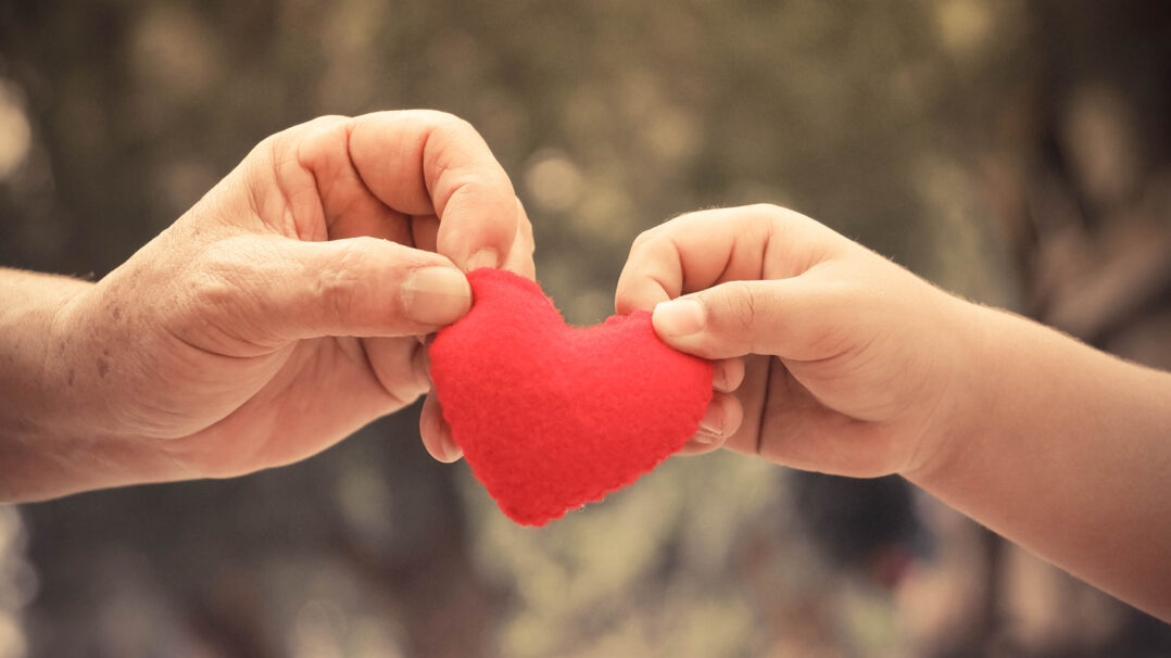 Aikuisen ja lapsen kädet pitelevät huovasta muotoiltua punaista sydäntä