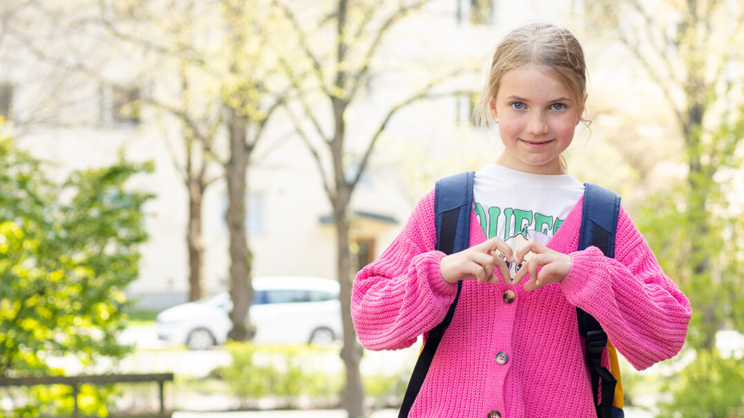 Tyttö hymyilee ulkona ja näyttää käsillään sydäntä