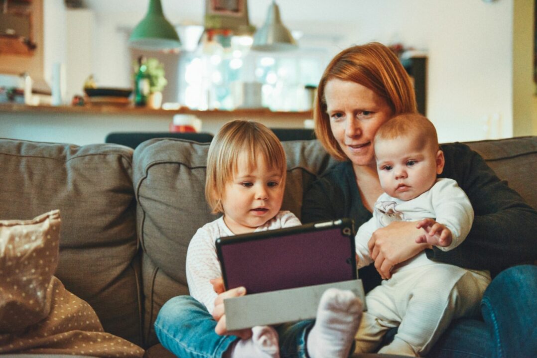 Kuvituskuva, jossa nainen tutkii kahden pienen lapsen kanssa tablettitietokonetta sohvalla.