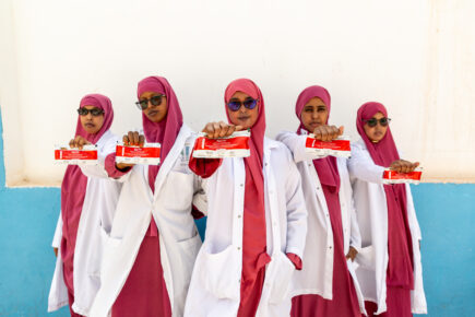 Viisi terveydenhoitajaa seisovat valkoisen seinän edessä kädessään runsasenergisiä maapähkinäpatukoita, jotka auttavat aliravitsemukseen.