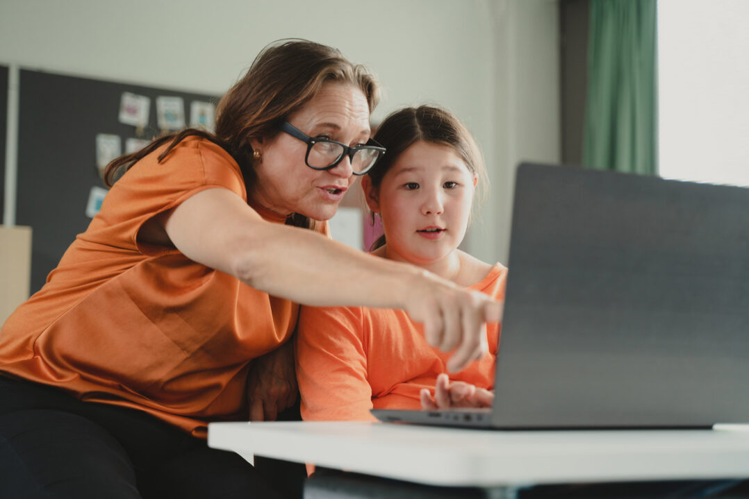 Kuvituskuva, jossa opettaja auttaa oppilasta kannettavan tietokoneen ääressä.