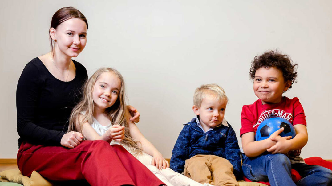 Nuori ja kolme nuorempaa lasta istuvat hymyillen vierekkäin lattialla