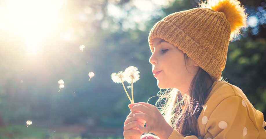 keltapipoinen tyttö puhaltaa kukan siemeniä