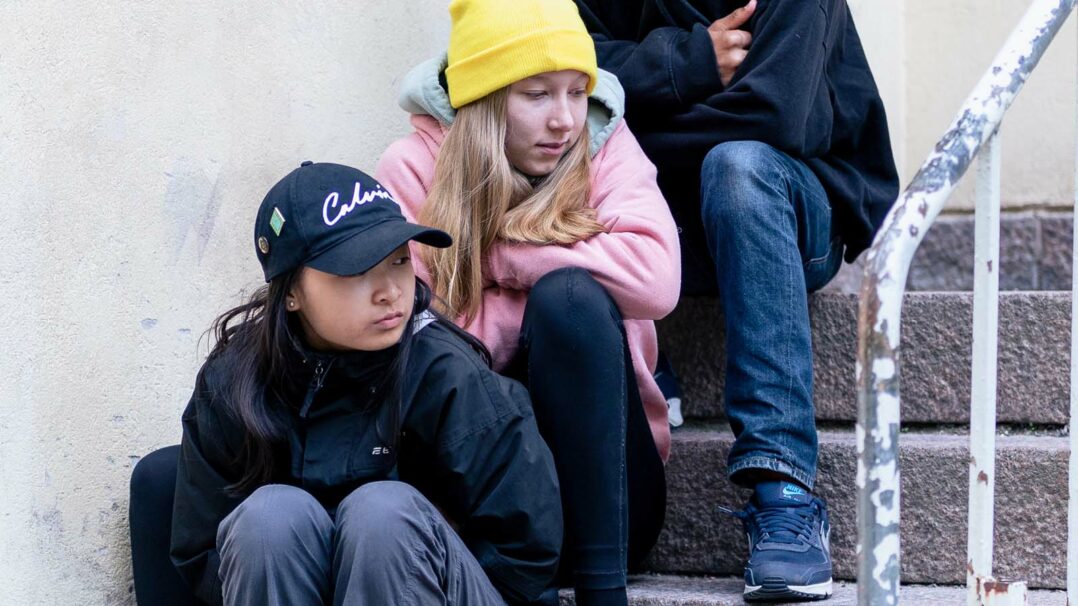 Nuoret istuvat koulun portailla.