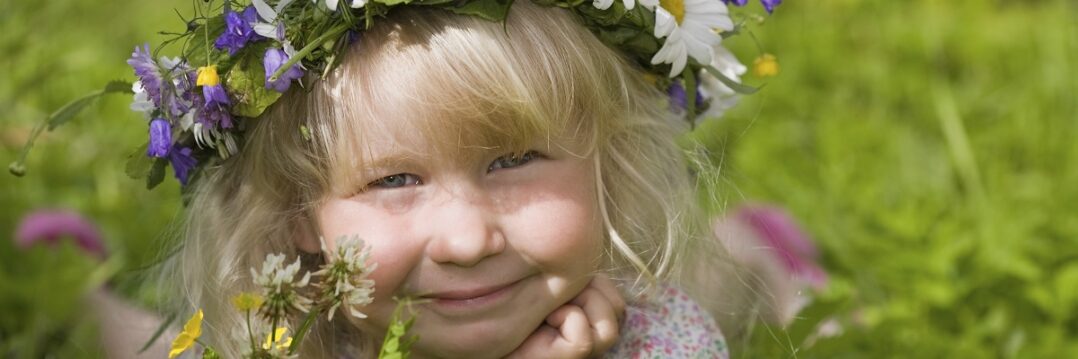 Iloinen lapsi niityllä kukkaseppele päässään.