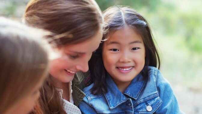 aasialainen tyttö istuu aikuisen naisen sylissä ja hymyilee