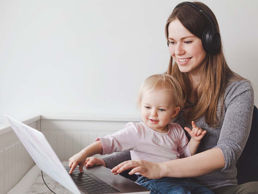 aikuinen kuulokkeet päässä ja lapsi sylissä katsovat kannettavaa tietokonetta