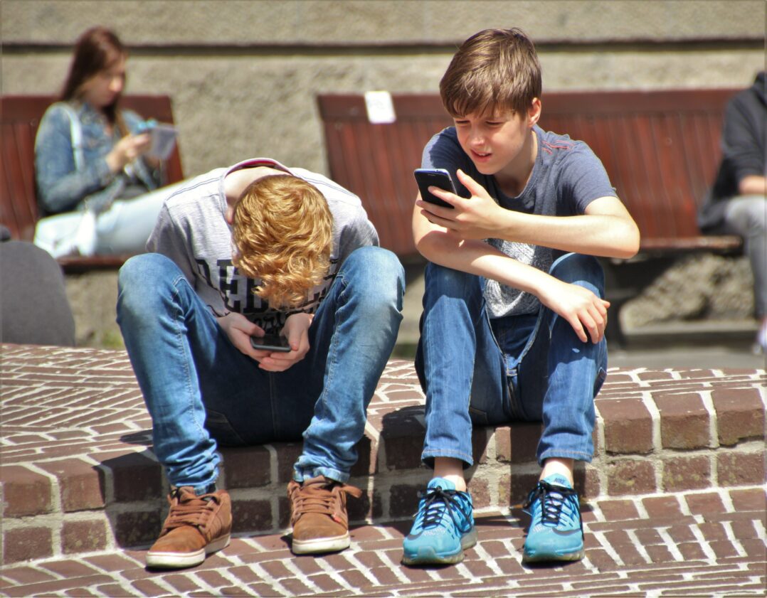 Kuvituskuva, jossa kaksi lasta istuu katukivetyksellä ja katsovat käsissään olevia älypuhelimia.