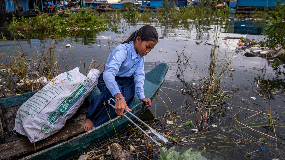 Tyttö keräämässä veneellä vedestä roskia Kambodzhassa.