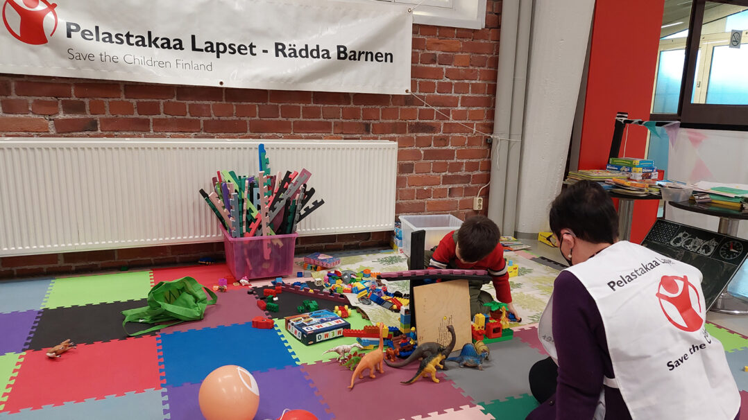 Lapsiystävällisessä tilassa Pelastakaa Lasten työntekijä leikkii kanssa legoilla.