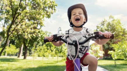 Pieni iloionen poika polkee pyörällä kohti kameraa ja nauraa suu auki
