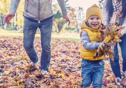 pikkupojalla kädet täynnä värikkäitä lehtiä perheen syksyisellä kävelyretkellä.