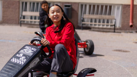 Tyttö ja poika ajamassa karting-autoilla pihalla.