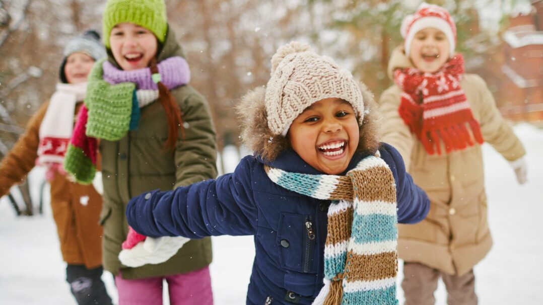 Iloisia lapsia värikkäissä talvivaatteissa lumisateessa.