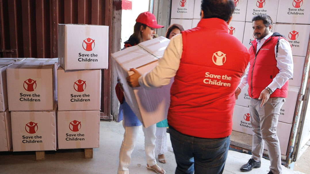 Save the Childrenin työntekijät kantavat tarvikkeita varastossa Pakistanissa.