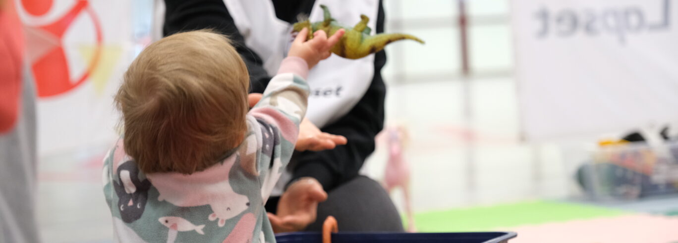 Lapsi ojentaa dinosauruslelua Pelastakaa Lapset -vapaaehtoiselle lapsiystävällisessä tilassa.