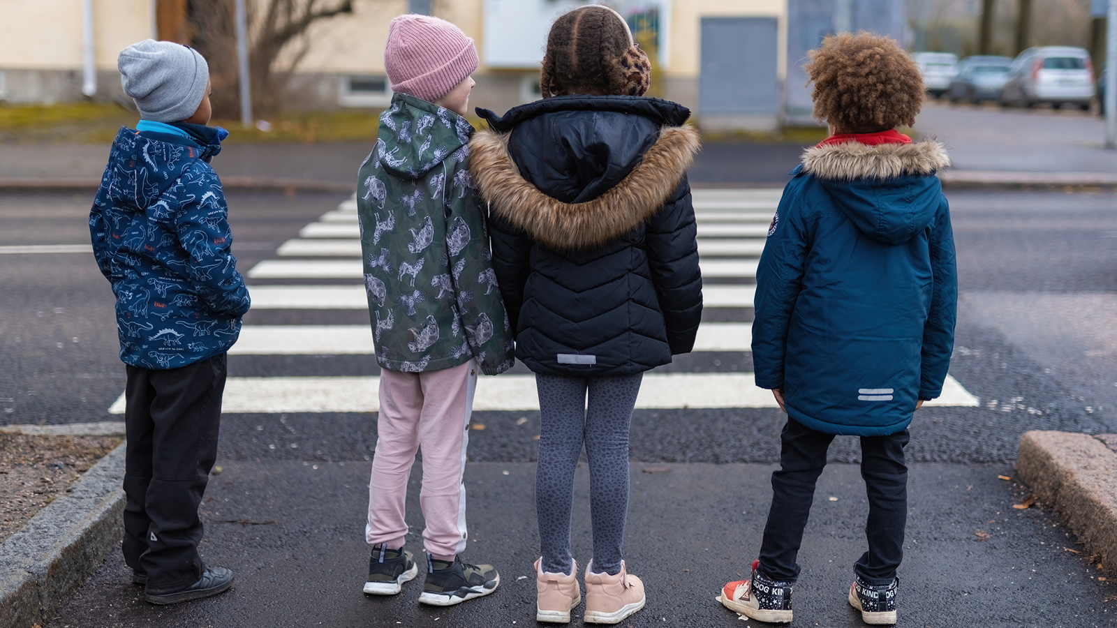 Neljä lasta seisomassa kadulla ja siirtymässä suojatielle syksyisessä maisemassa Suomessa.