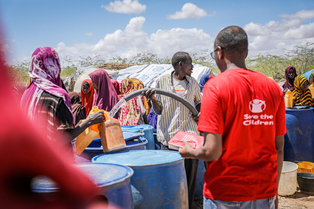 Pelastakaa Lasten työntekijä jakaa vettä Somaliassa ihmisille, jotka jonottavat taustalla.