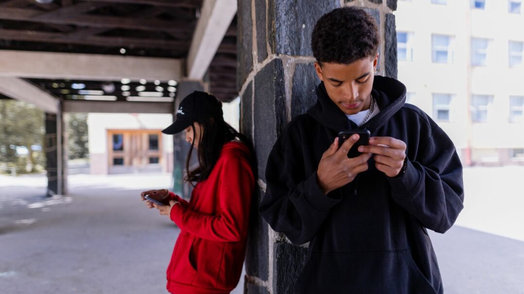 Kaksi nuorta koulun pihalla katsomassa puhelimiaan