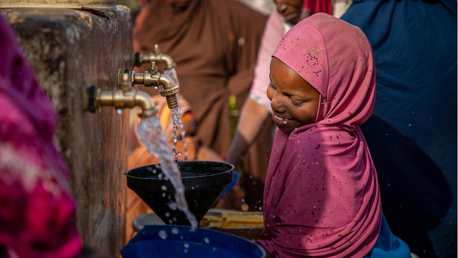 Hymyilevä tyttö ottaa vettä kanisteriin Somaliassa