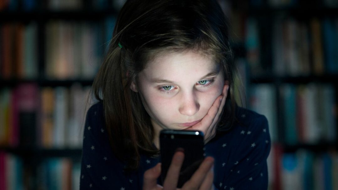 Nuori tyttö pimeässä huoneessa katsoo kännykkää.