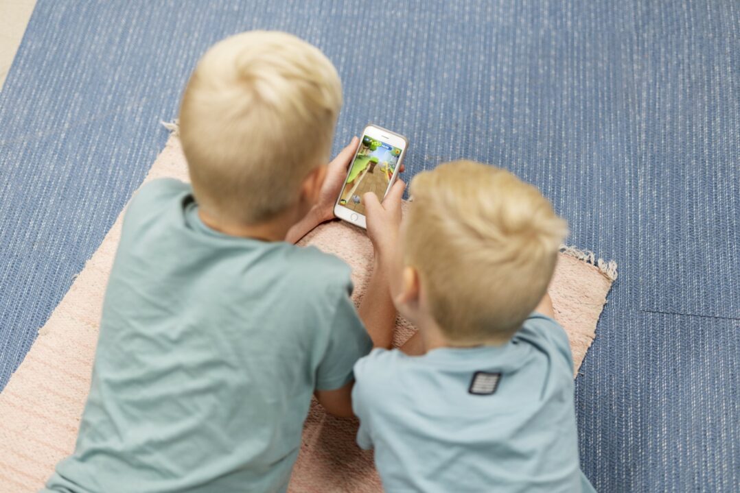 Kaksi lasta katsoo älypuhelinta maassa makoillen.