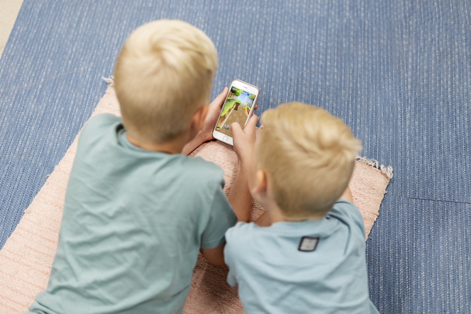 Kaksi lasta katsoo älypuhelinta maassa makoillen.