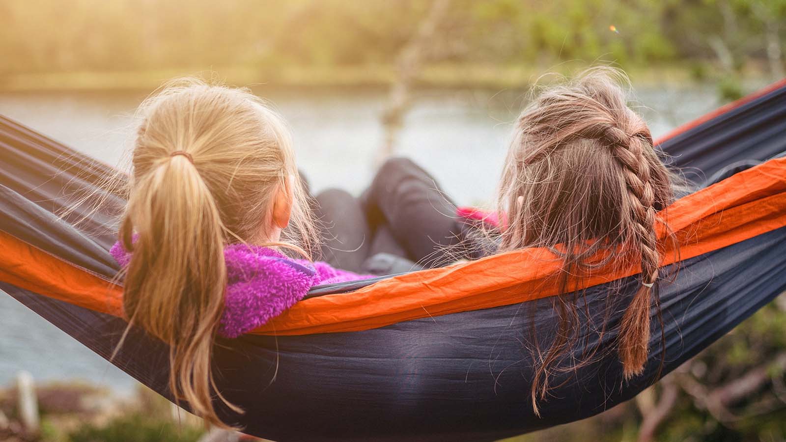 kaksi tyttöä istuu riippukeinussa ja katselee järvelle