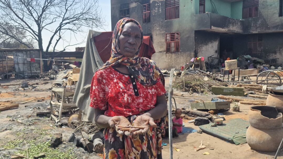 Nainen tuhoutuneen rakennuksen edessä pitää käsissään luoteja.