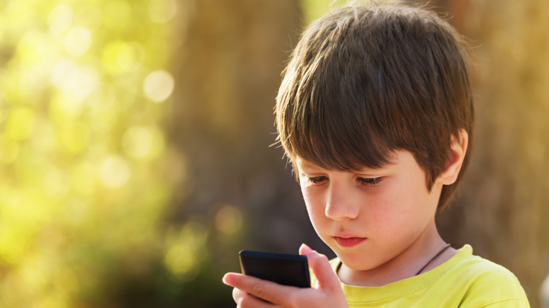 Lapsi selaa älypuhelinta syksyisessä maisemassa.