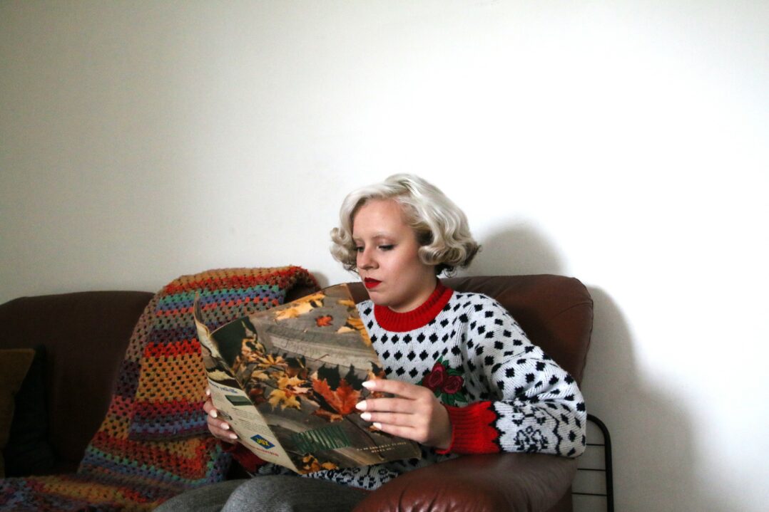 Tyttö lukee lehteä sohvalla istuen