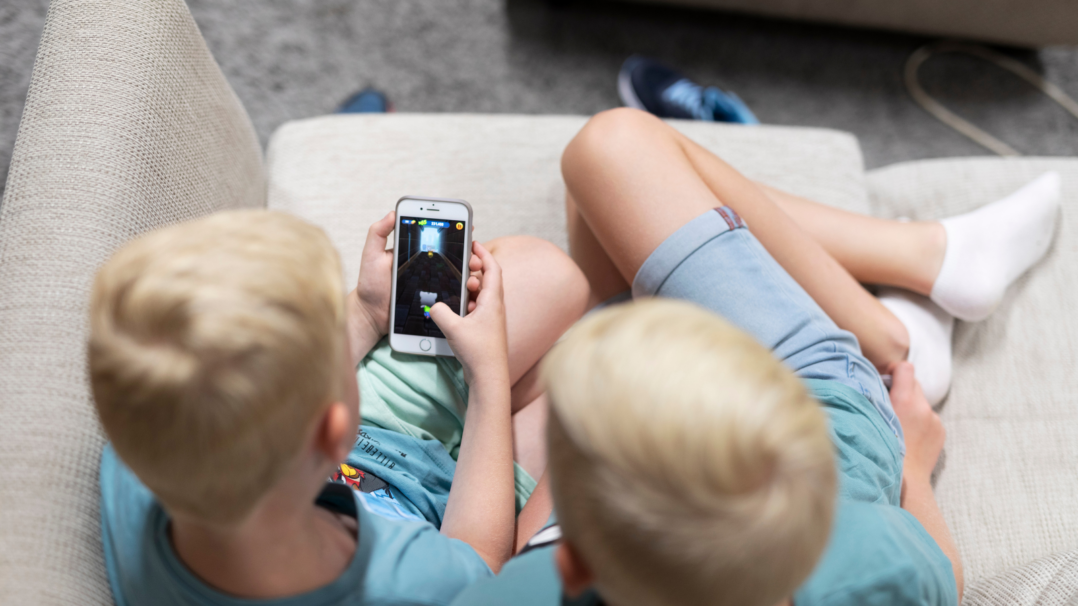 Kaksi lasta istuu sohvalla ja pelaa älypuhelimella.