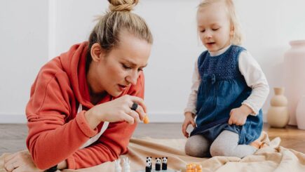 Nutturapäinen nainen hupparissa pelaa tyttölapsen kanssa peliä lattialla