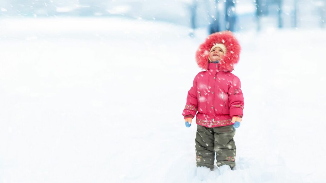 Lapsi vaaleanpunaisessa takissa seisoo lumisateessa.