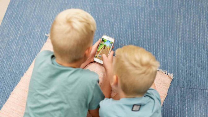 Kaksi lasta lattialla pelaamassa älypuhelimella.