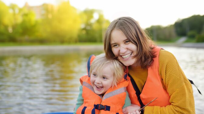 Nainen ja lapsi hymyilevät pelastaliivit päällä veneessä.