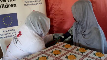 Pelastakaa Lasten kätilö mittaa naisen verenpainetta terveyskeskuksessa Sudanissa. Taustalla EU:n logo.
