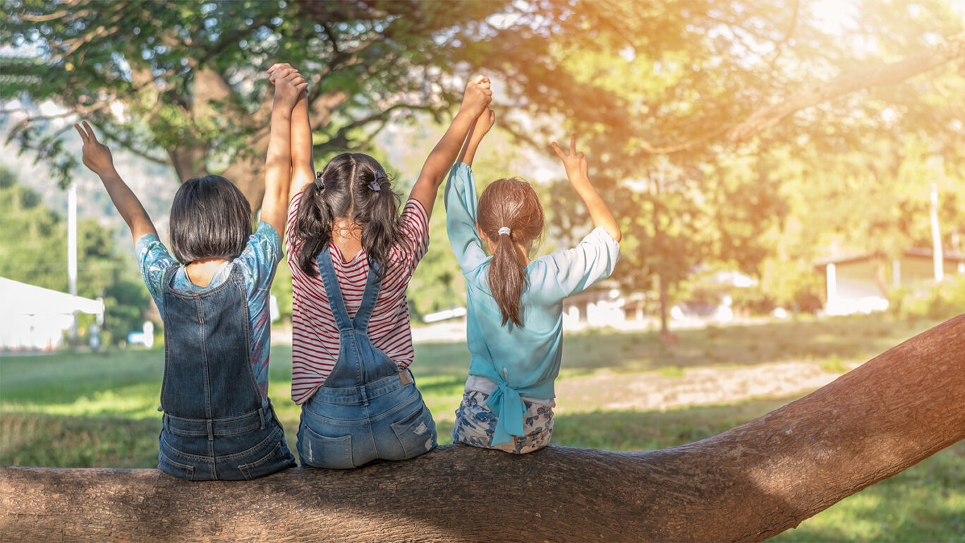 Kolme lasta istuu puun rungon päällä