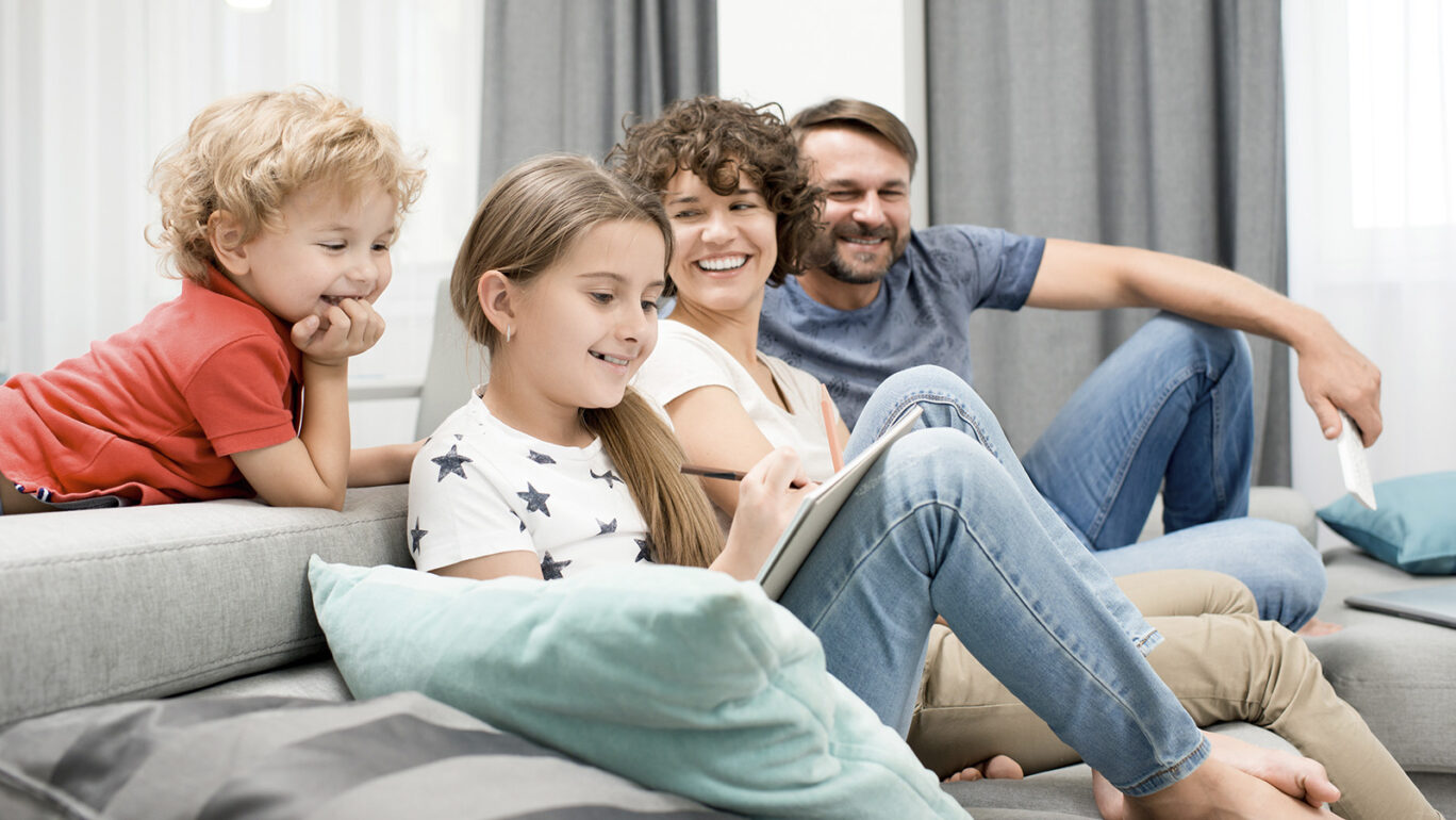 perheen lapset ja vanhemmat istuvat sohvalla yhdessä