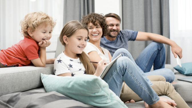 perheen lapset ja vanhemmat istuvat sohvalla yhdessä