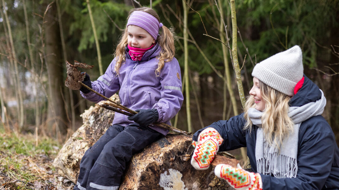 Aikuinen ja lapsi istuvat yhdessä metsässä ja tutkivat kaarnan paloja