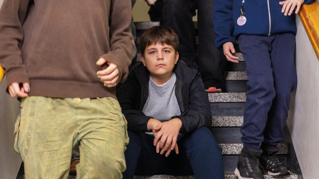 Lapsi istuu koulun portailla ja katsoo kameraan